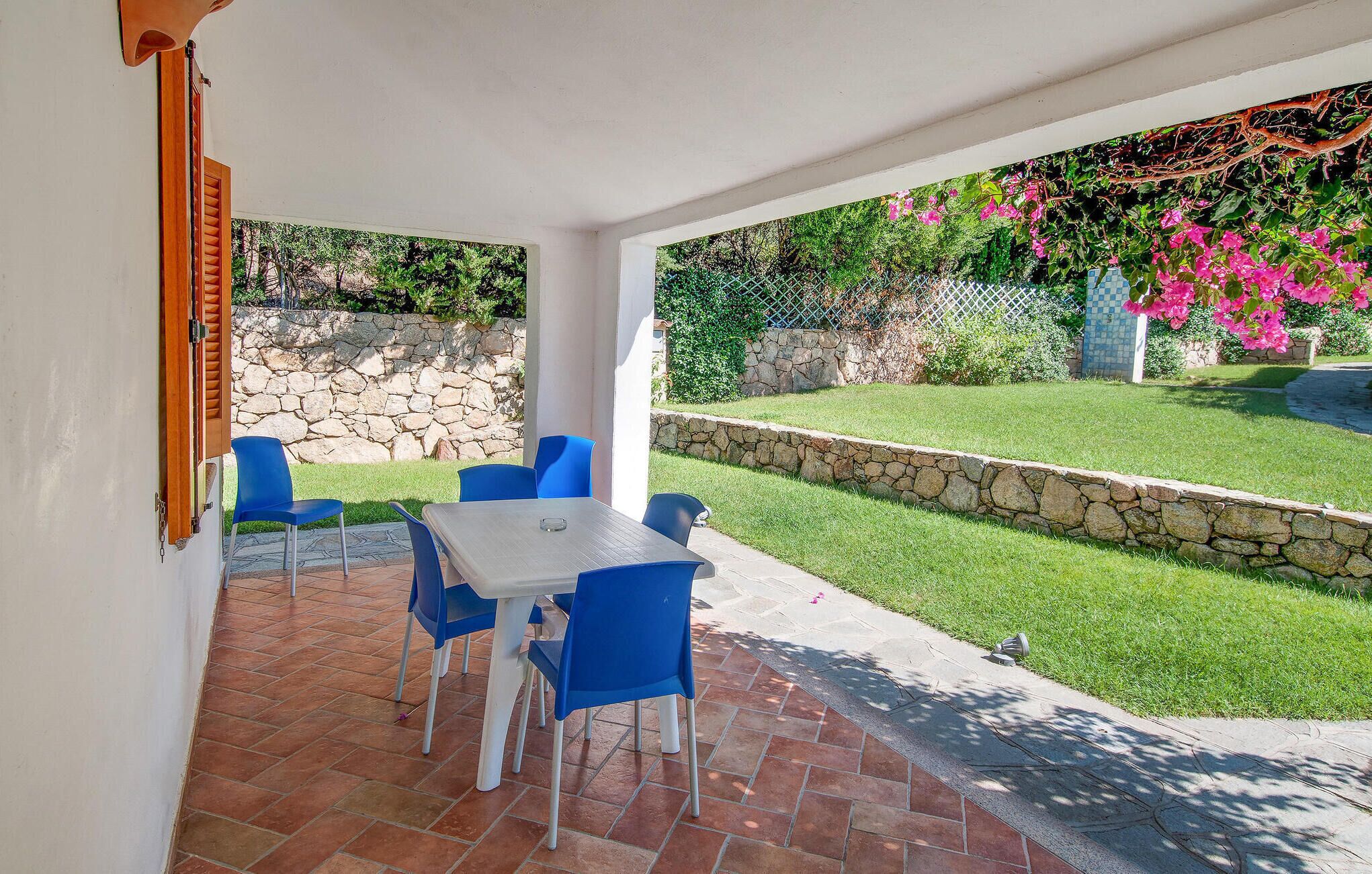A patio with a table and blue chairs, a stone wall, and a grassy area with pink flowers.