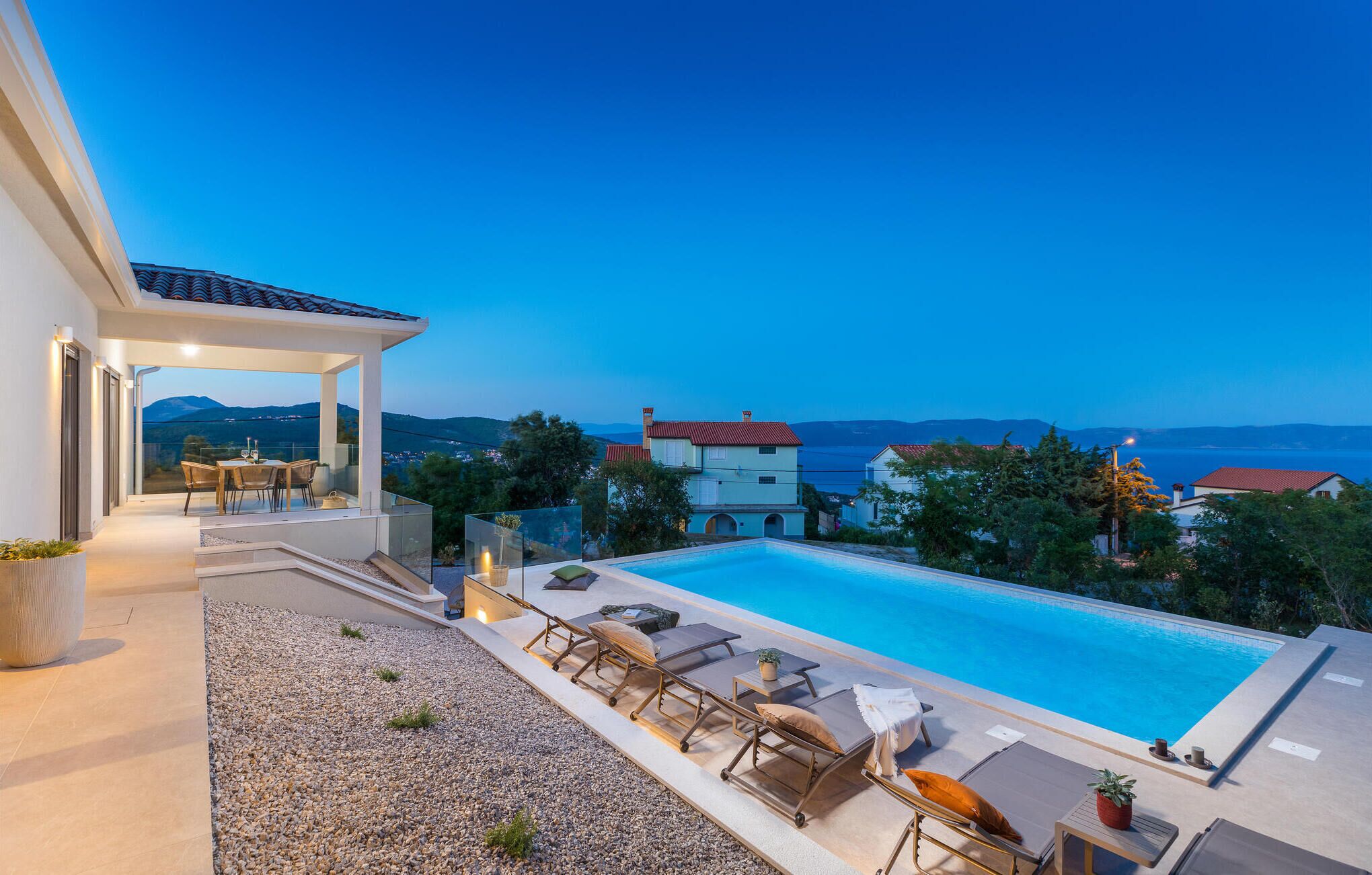 Un espace piscine aménagé sur le toit, avec des chaises longues et une table, offrant une vue panoramique sur la mer et les montagnes.