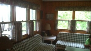 A cozy room with a checkered sofa, a small table, and a window with curtains. - Secluded Hillside Property with Valley Views and Fishing Pond (Burlington Flats)