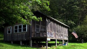 A rustic wooden cabin with a porch, surrounded by lush greenery. - Secluded Hillside Property with Valley Views and Fishing Pond (Burlington Flats)