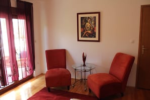 Quarto com duas poltronas vermelhas, uma mesa de vidro com um objeto decorativo e um quadro na parede.