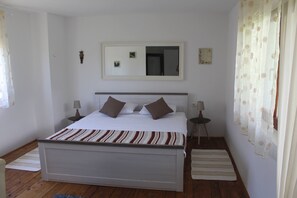 Quarto com uma cama de solteiro, duas mesas de cabeceira, um espelho e uma janela com cortinas.