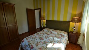 Une chambre à coucher avec une couvre-lit à motifs floraux, une armoire en bois, une lampe de chevet et un mur à rayures.