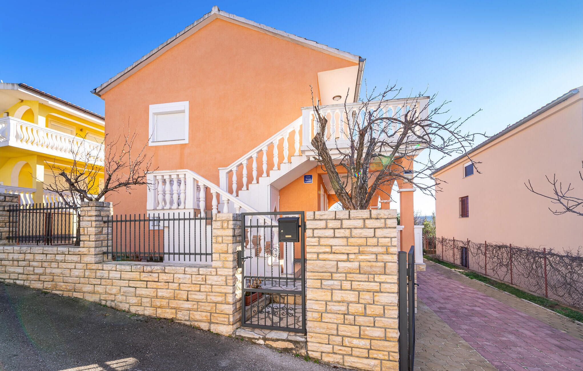 A two-story building with a stone wall entrance, a white staircase, and a balcony.