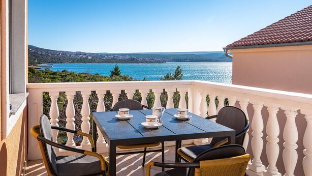 A balcony with a table and chairs, overlooking a body of water and a distant town. - 2 bedroom cozy apartment in Krusevo (Krusevo)