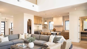 A spacious living area with a grey sectional sofa, a coffee table, and a dining area with wooden cabinets and a kitchen in the background. - Golden Hour by RedAwning (St. George)