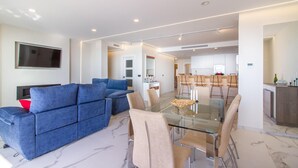 A modern living room with a blue sofa, a glass dining table, and a kitchen in the background. - Awesome apartment in Santa Pola with WiFi (Santa Pola)