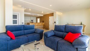 A modern living room with two blue sofas, a glass coffee table, and a kitchen in the background. - Awesome apartment in Santa Pola with WiFi (Santa Pola)