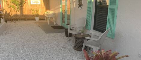 Un patio con pared blanca, contraventanas verdes y mobiliario exterior.