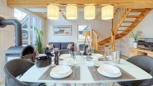 A dining area with a white table set for four, surrounded by grey chairs. There is a wooden staircase to the right and a large window with a view of the outside. - Awesome home in Zerpenschleuse with sauna (Zerpenschleuse)