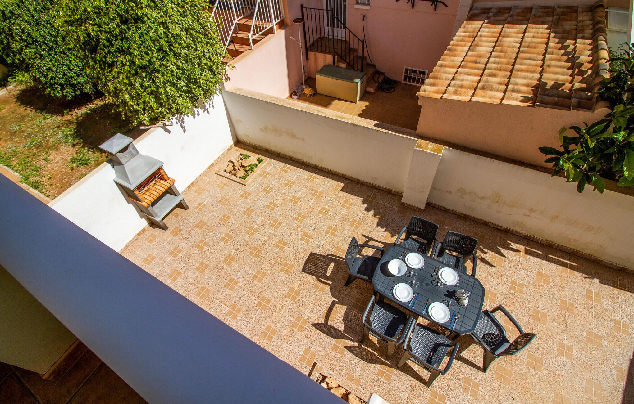An outdoor patio with a round table and chairs, surrounded by a tiled floor and a white wall.