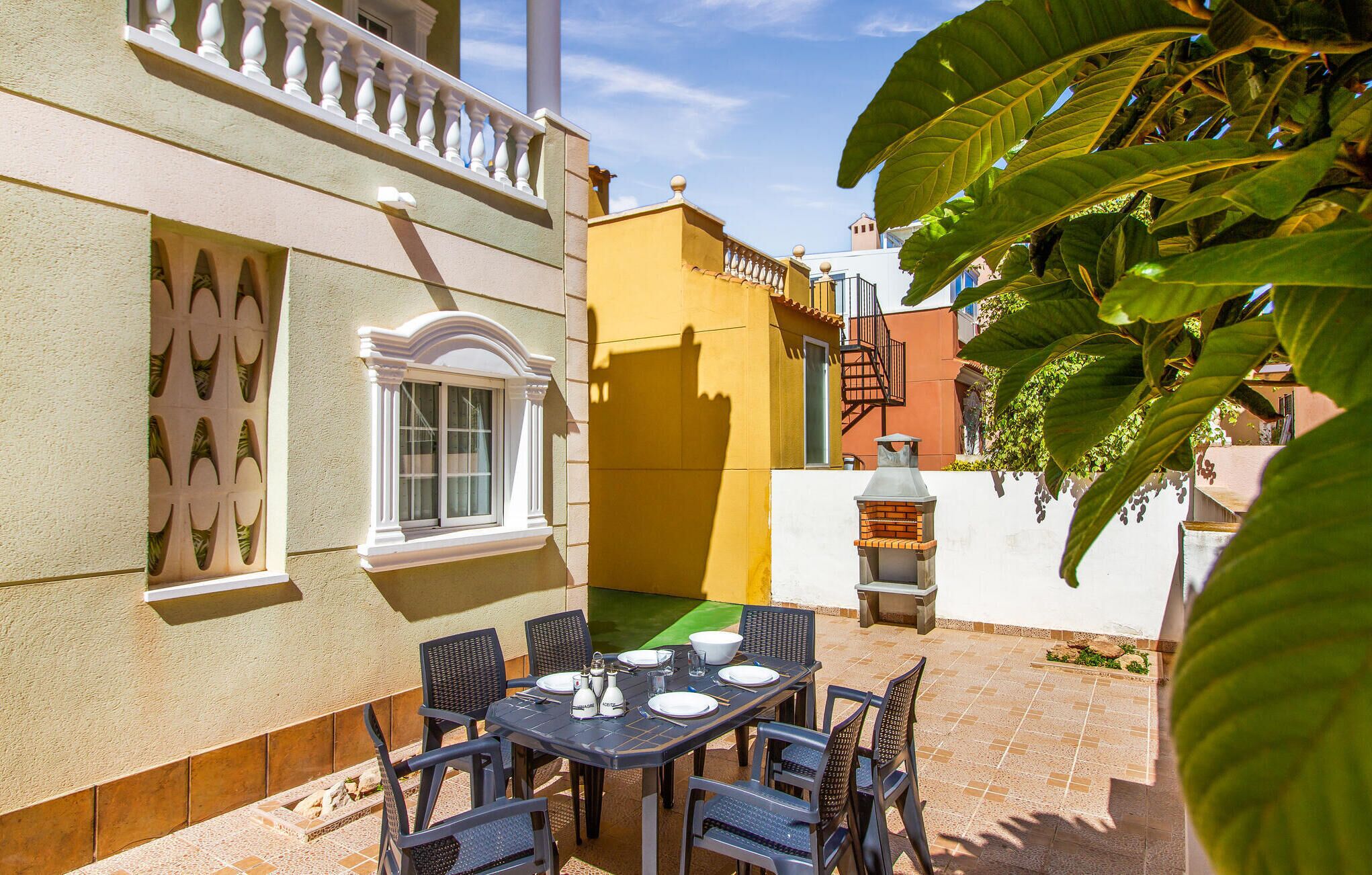 A patio with a table set for dining, surrounded by chairs, and a barbecue grill.