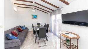 Un espacio habitable compacto con comedor, un sofá gris con cojines estampados, un televisor montado en la pared y una mesa de madera con un florero.