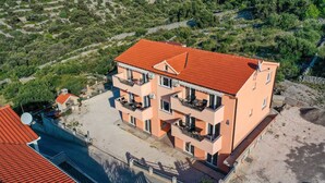 Un edificio de varios pisos con techo de tejas rojas, balcones y un paisaje circundante.