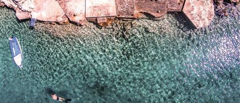 A clear view of a rocky shoreline with a boat anchored near the shore and a person swimming in the water.