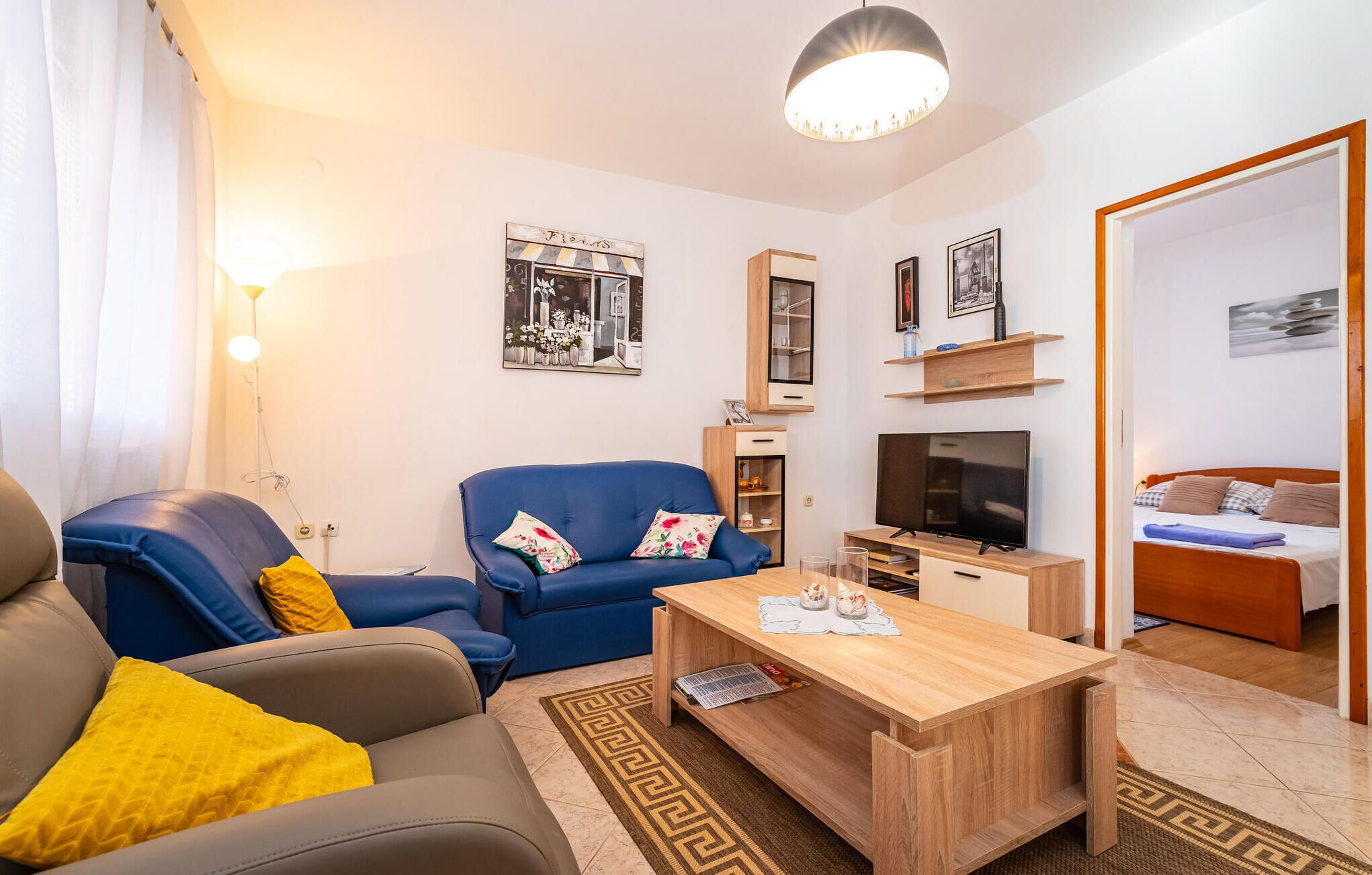 Een moderne woonkamer met een bank, fauteuil, salontafel, televisie en een bed op de achtergrond.