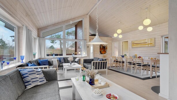 Un salón amplio con un sofá grande, un comedor con mesa y sillas, y una cocina al fondo.