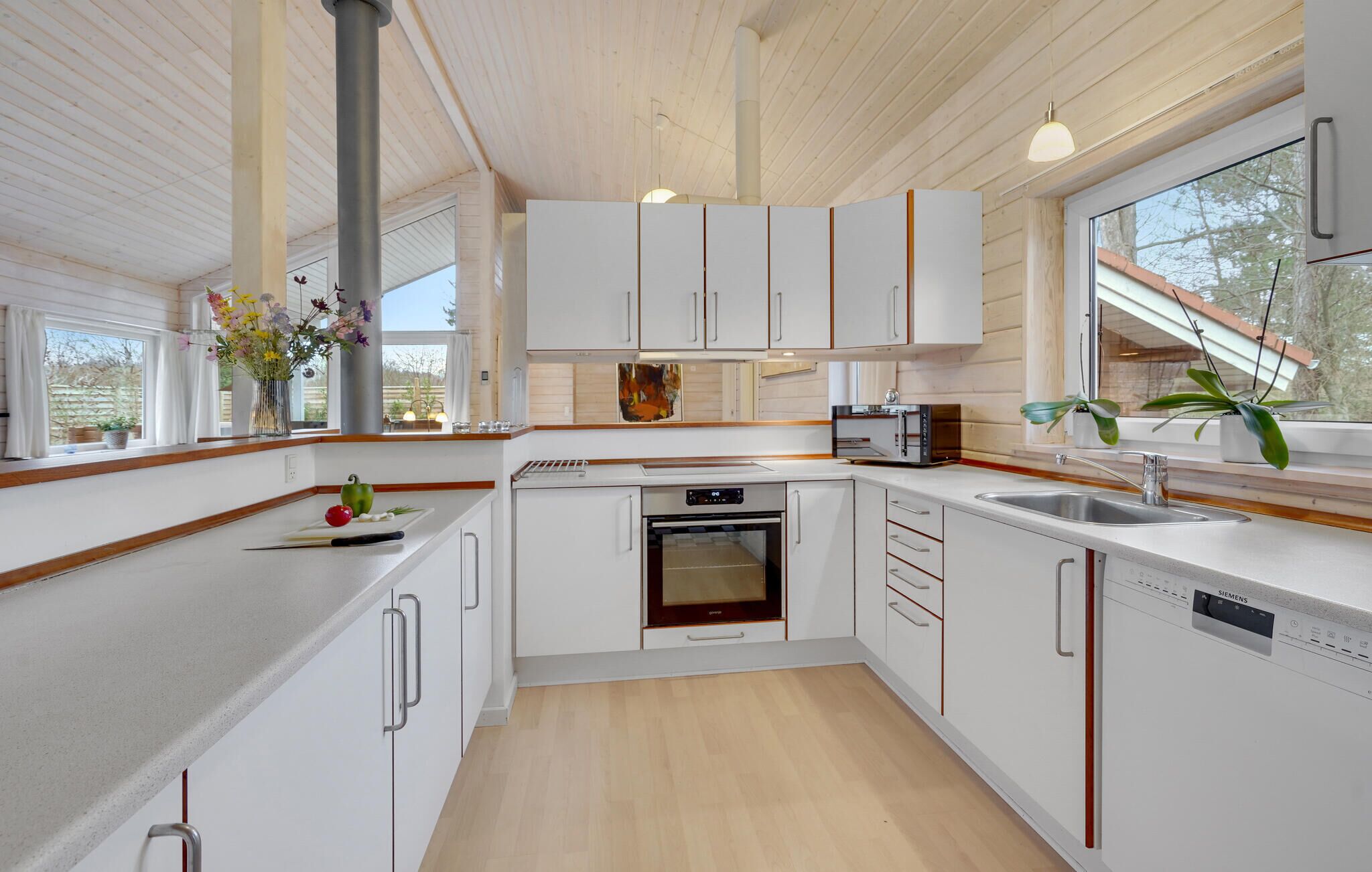 A modern kitchen with white cabinets, a built-in oven, a dishwasher, and a large window providing natural light.