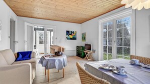 Une pièce spacieuse avec un plafond en bois, de grandes fenêtres, une table à manger dressée pour le thé et un coin salon confortable.
