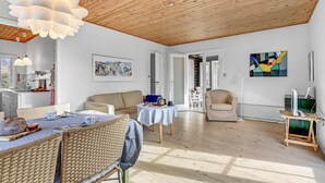 Un vaste espace de vie doté d’un haut plafond en bois, d’une table à manger avec des chaises, d’un canapé et d’une petite table recouverte d’une nappe.