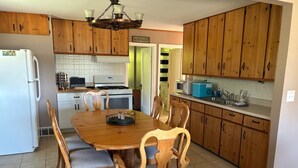 Uma cozinha com armários de madeira, uma mesa de jantar com cadeiras, uma geladeira, um fogão e um micro-ondas.