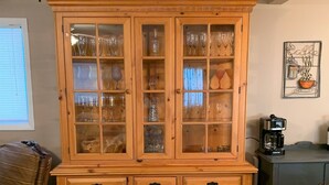 Um armário de madeira com portas de vidro, gavetas e uma máquina de café sobre uma mesa.