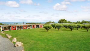 A row of red-roofed buildings with large windows and a grassy field in the foreground.