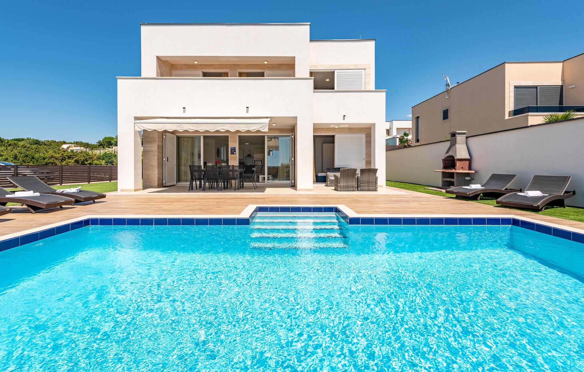 A modern two-story house with a swimming pool, outdoor seating, and a barbecue area.