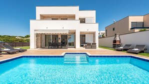 Une maison moderne à deux étages dotée d’une piscine, d’un espace salon extérieur et d’un coin barbecue.