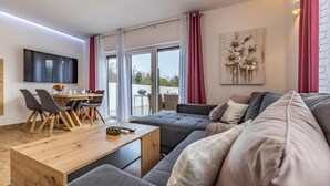 A modern living room with a sofa, a dining table with chairs, a flat-screen TV, and a large window with curtains. - Beautiful home in Medulin (Medulin)