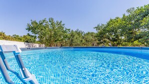A swimming pool with clear blue water, surrounded by trees and a concrete wall. - Beautiful home in Medulin (Medulin)