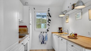 Eine kompakte Küche mit weißen Schränken, einem Fenster mit Blick, einer Kaffeemaschine und einer Obstschale auf der Arbeitsplatte.