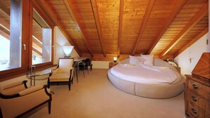 A bedroom with a wooden ceiling, a round bed, a desk, and a chair. - Grand Maisonette-Attica, Jenins, Top of Heidiland (Jenins)