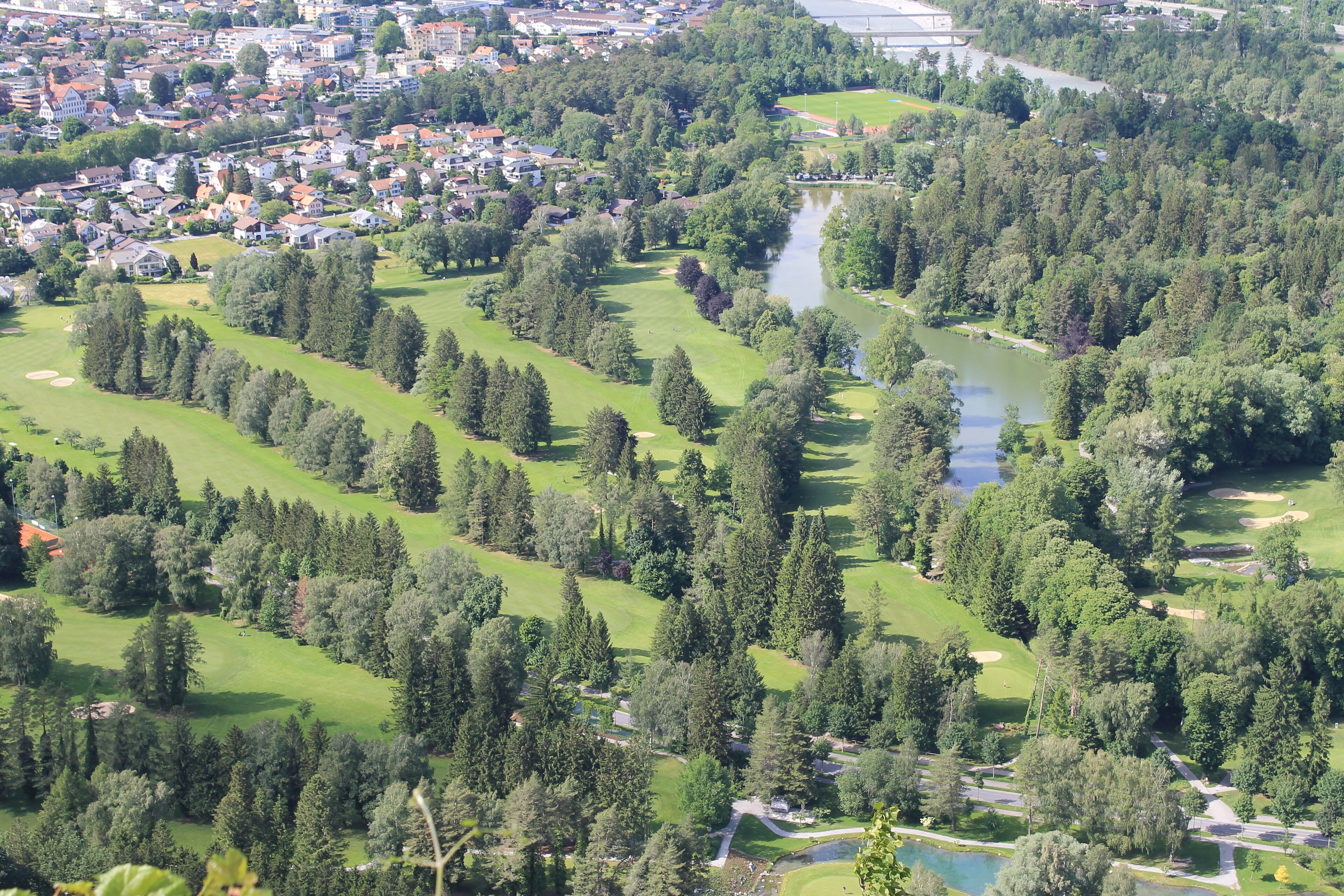 An aerial view of a golf course with multiple fairways, a water body, and surrounding residential areas.