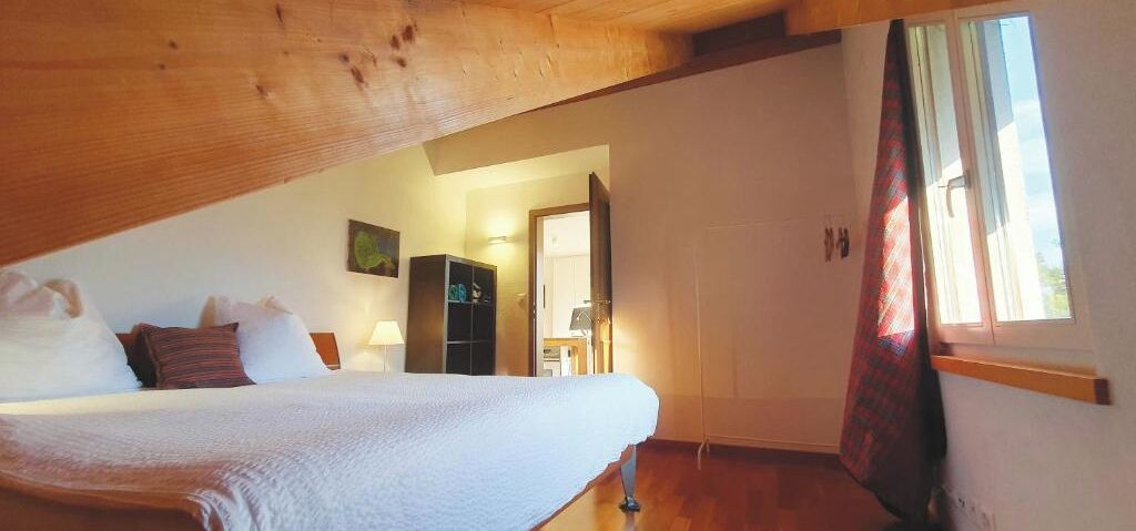 A bedroom with a bed, a wardrobe, a desk, and a window with curtains.