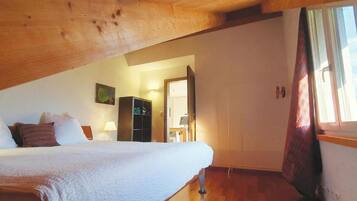 A bedroom with a bed, a wardrobe, a desk, and a window with curtains.