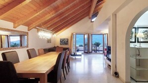 A spacious dining area with a wooden table and chairs, a chandelier, and a view through large glass doors to an outdoor patio. - Grand Maisonette-Attica, Jenins, Top of Heidiland (Jenins)