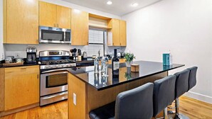 A modern kitchen with wooden cabinets, stainless steel appliances, a central island with bar stools, and a window with blinds. - Houston Getaway by Downtown | Pool Table | Pets (Houston)