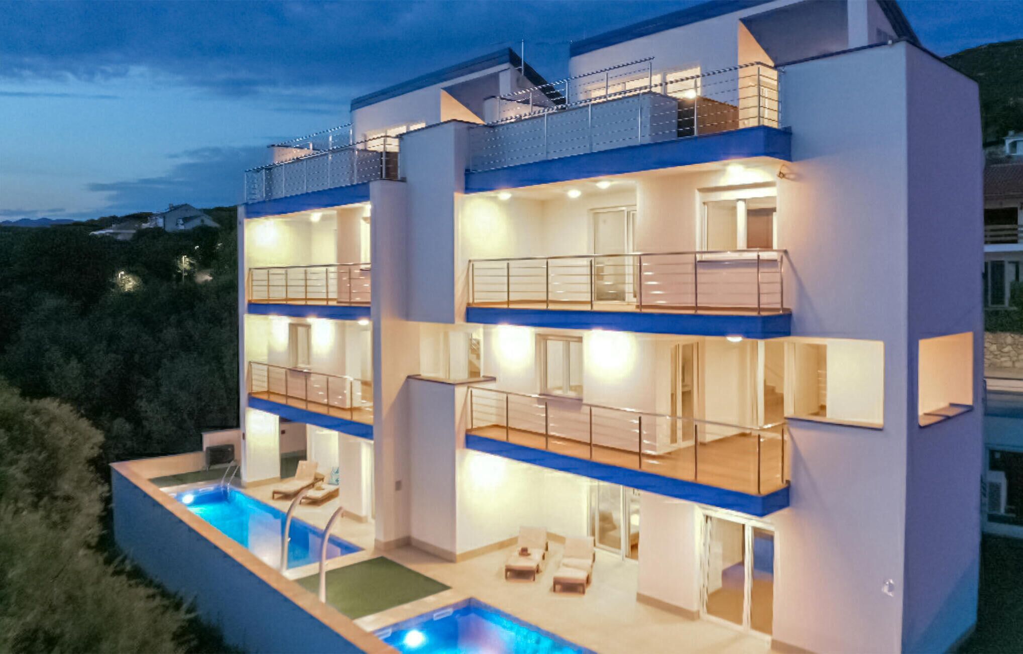A multi-story modern building with balconies, a swimming pool, and a well-lit interior.