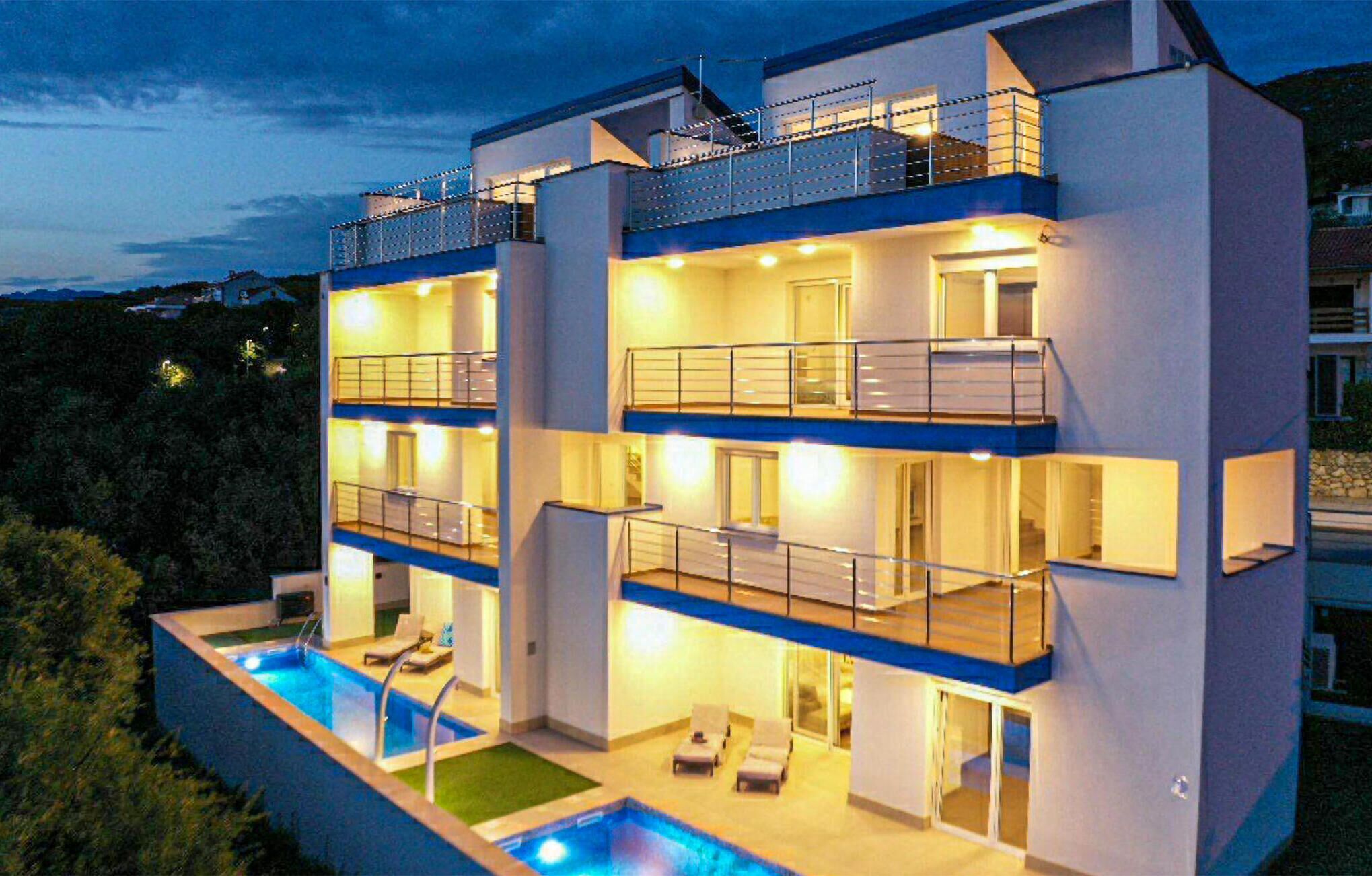 A modern multi-story building with a swimming pool, balconies, and a well-lit interior.