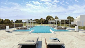A pool area with lounge chairs and umbrellas, surrounded by a stone wall and greenery.