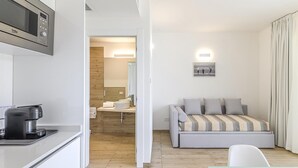 A compact hotel room with a kitchenette, a bed with a striped blanket, a small table, and a wall-mounted TV.
