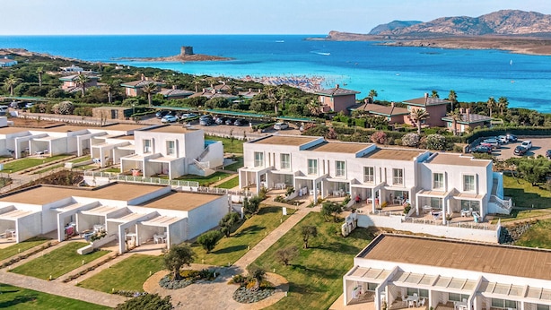 A coastal resort with modern villas, a beach, and a historic tower.
