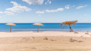 A beach with three thatched umbrellas and a palm tree.