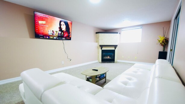 Uma sala de estar com um sofá branco, uma mesa de centro, uma lareira e uma TV na parede exibindo a interface da Netflix.