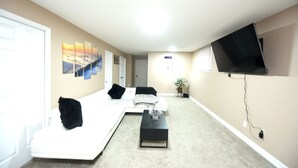 Sala de estar com sofá branco, mesa de centro, televisão de tela plana na parede e um quadro na parede.