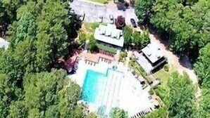 An aerial view of a property with a swimming pool, tennis court, and surrounding greenery.