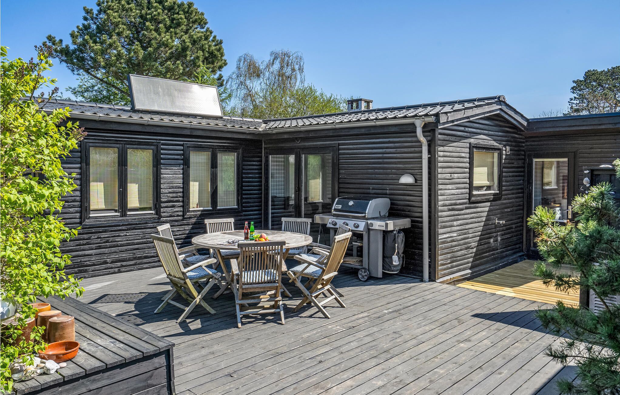 En træhytte med terrasse, grill og et bord med stole.
