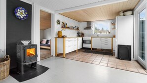 A modern kitchen with white cabinetry, a wood-burning stove, and a large window. - Beach front home in Nykøbing Sj with WiFi (Nykøbing Sj)