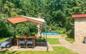 A patio with a table and chairs, a covered area, and a swimming pool in the background.